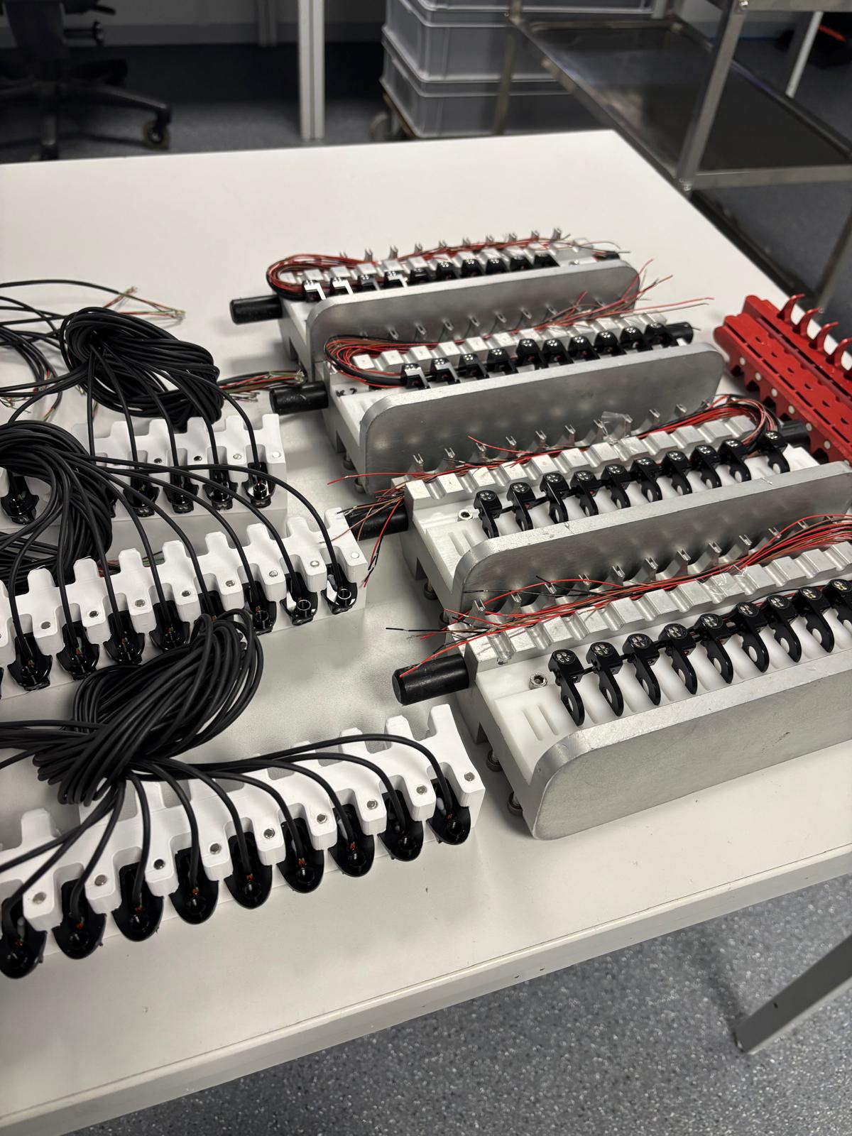 Custom 3D-printed and machined cable/connector fixtures laid out on a workbench