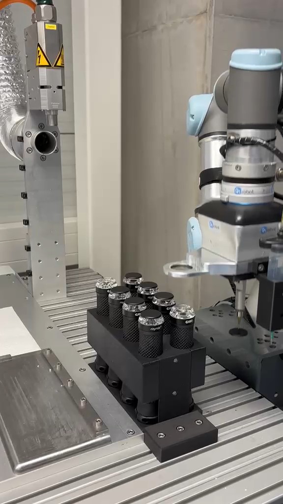Collaborative robot with a dispensing tool beside a black fixture holding indicator components, still frame from project footage
